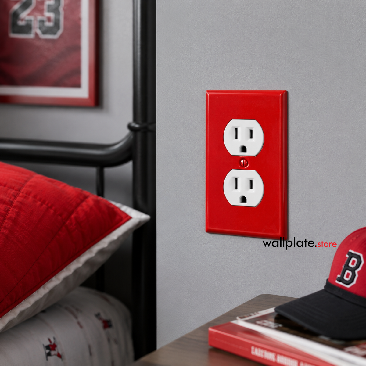 A red rectangular wall plate cover with two white US electrical outlet cutouts, mounted on a gray wall in a bedroom.